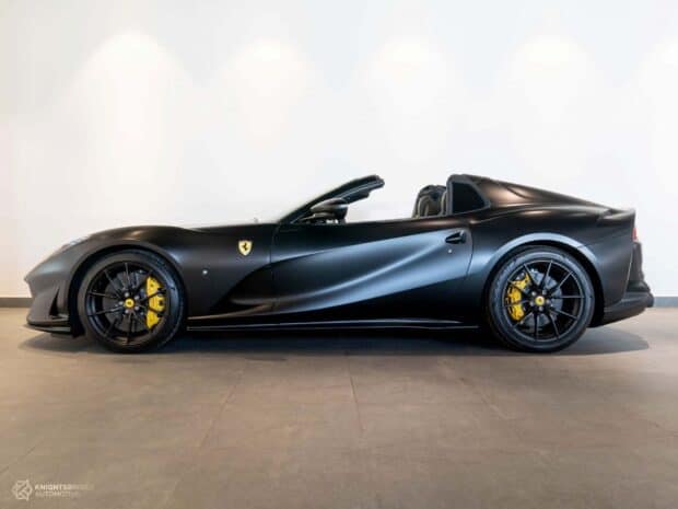 A sleek black Ferrari 812 Gts is displayed in a showroom with yellow brake calipers and convertible top, HD Desktop Wallpaper