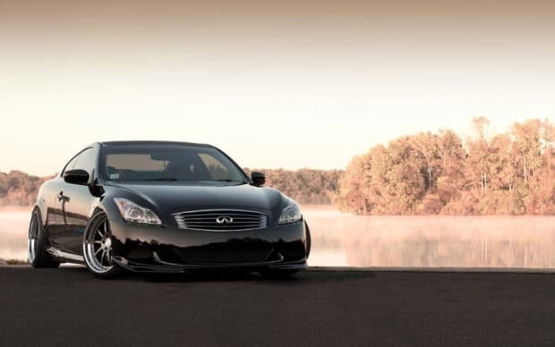 A sleek black Infiniti G37 is parked near a calm lake with autumn trees in the background, HD Desktop Wallpaper
