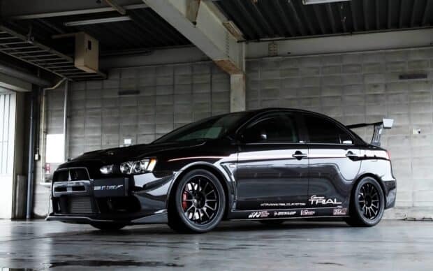 A sleek black Lancer Evo is parked inside a concrete garage with racing decals, 2K Desktop Wallpaper