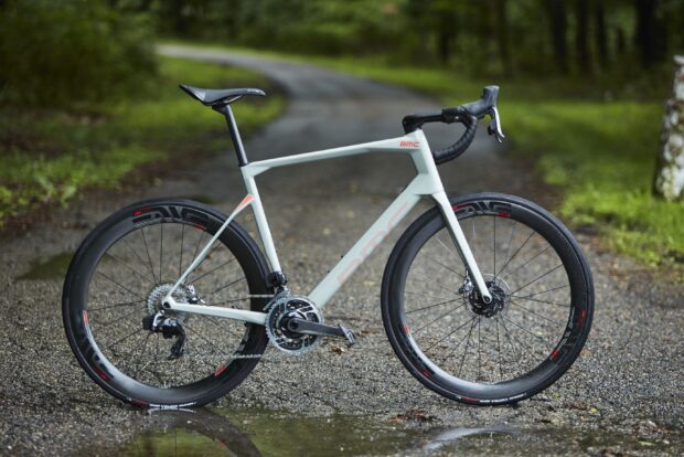 A sleek Bmc bike stands on a forest path with gravel and greenery, 2K Desktop Wallpaper