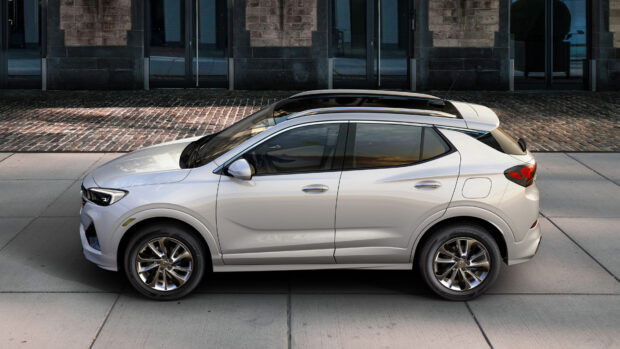 A silver Buick Encore is parked on the street next to a brick building under clear light, 4K Desktop Wallpaper