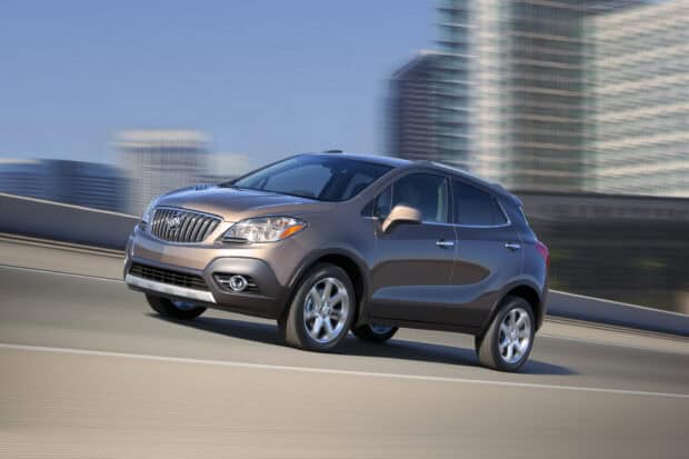A sleek Buick Encore drives along a city highway with blurred buildings in the background, 2K Desktop Wallpaper