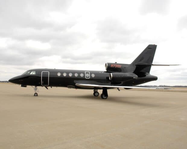 A sleek Dassault Falcon 50 jet is parked on an empty runway under a cloudy sky, HD Desktop Wallpaper