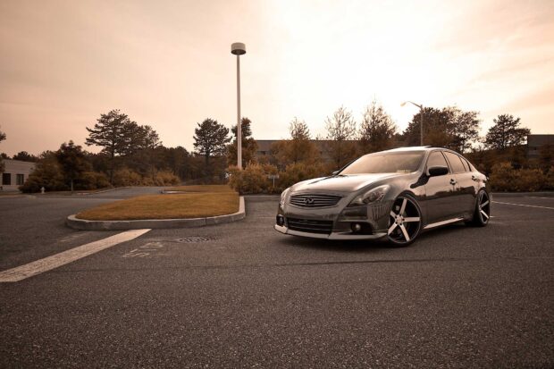 A black Infiniti G37 is parked in an empty lot with scenic trees and buildings in the background, HD Desktop Wallpaper