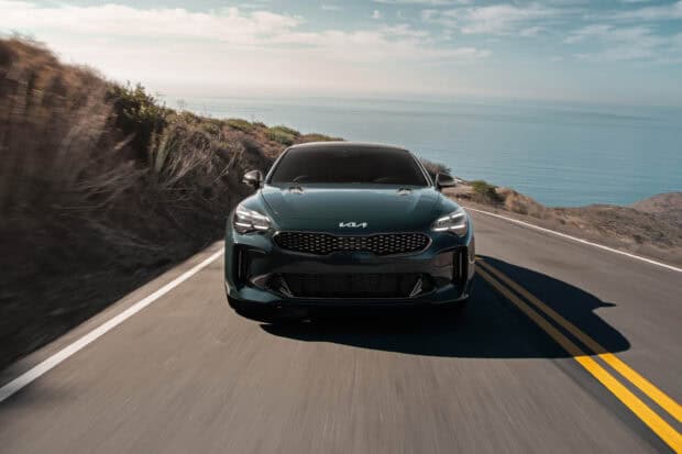A sleek Kia car is driving on a coastal road with the ocean in the background, 2K Desktop Wallpaper