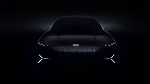 A sleek Kia car is shown from the front with illuminated headlights and logo in dark lighting, HD Desktop Wallpaper