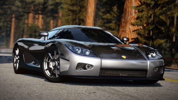 A sleek Koenigsegg sports car is parked on a forest road surrounded by tall trees, 2K Desktop Wallpaper