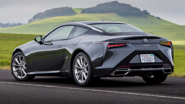 A sleek dark Lexus LC is parked on an open road with green hills in the background showing its elegant design, HD Desktop Wallpaper