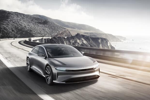 A sleek Lucid Motors car drives along a winding coastal highway with mountains and ocean in the background, 2K Desktop Wallpaper