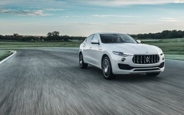 A white Maserati Levante is driving swiftly on a curved race track during the day, 2K Desktop Wallpaper