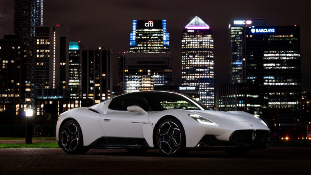A white Maserati Mc20 is parked with city skyscrapers glowing at night, 4K Desktop Wallpaper