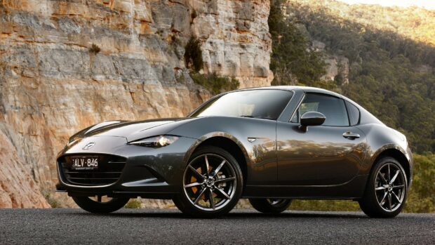A gray Mazda MX 5 Miata drives by rock cliffs in a scenic outdoor setting, HD Desktop Wallpaper