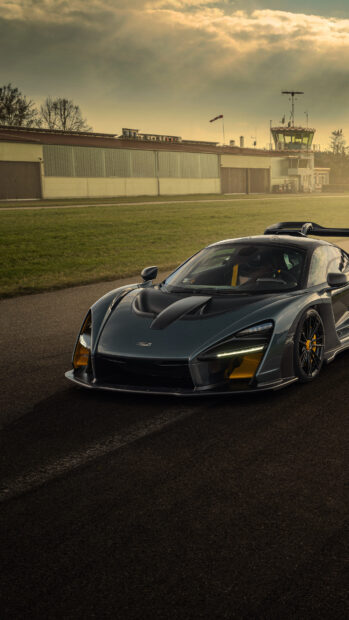 A McLaren Senna car stands on a racetrack near a building under a cloudy sky, 4K Phone Wallpaper