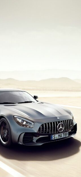 A silver Mercedes Benz AMG GT is driving on a desert road with mountains in the background, 2K Phone Wallpaper