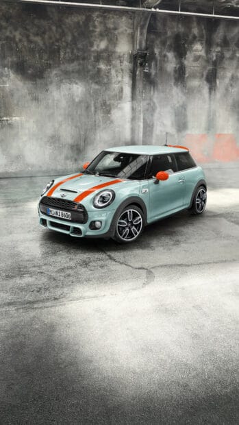 A light blue Mini Cooper with orange accents is parked on a textured surface inside a rustic warehouse, HD Phone Wallpaper