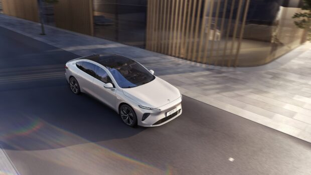 A sleek white Nio Auto is driving smoothly on an urban street, showcasing modern design, 2K Desktop Wallpaper