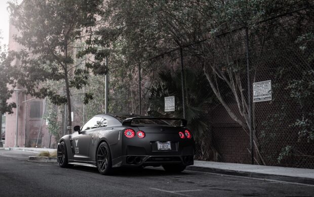 A matte black Nissan GT R is parked on a quiet city street near trees and fences, HD Desktop Wallpaper