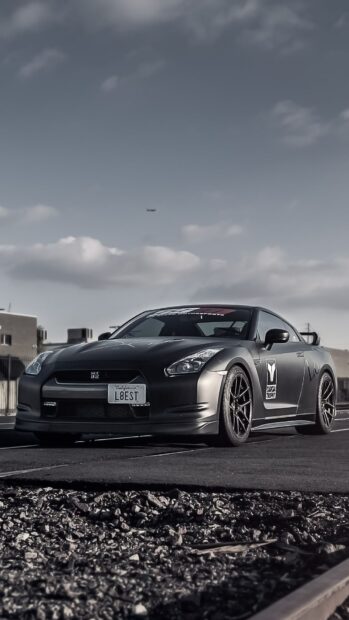 A sleek Nissan GT R racing on a street under a cloudy sky with urban buildings in the background, HD Phone Wallpaper