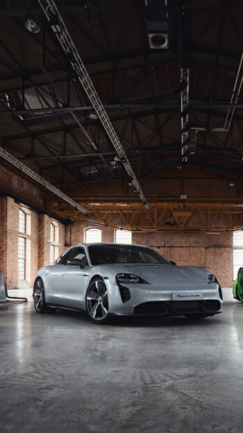 A silver Porsche Taycan Turbo is parked inside a spacious industrial building with large windows, 4K Mobile Wallpaper