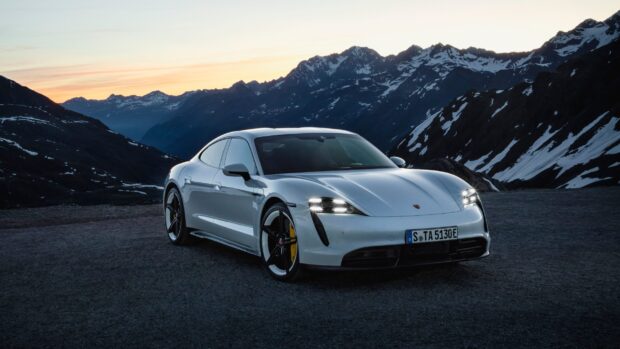 A sleek Porsche Taycan is parked with snow capped mountains at sunset, 2K Desktop Wallpaper