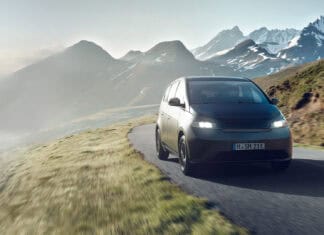 A Sono Motors vehicle drives along a windy mountain path with snow capped peaks in the background, HD Desktop Wallpaper