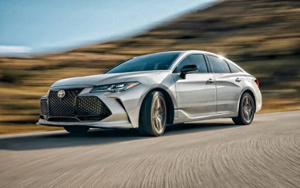 A silver Toyota Avalon car drives smoothly on a winding road through a dry landscape, 2K Desktop Wallpaper