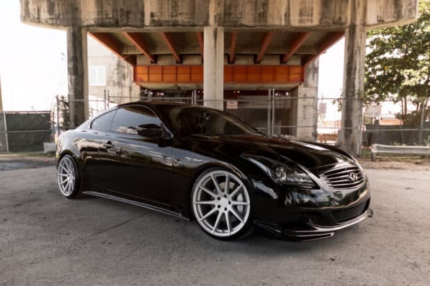A sleek black Infiniti G37 coupe is parked under an industrial overpass with custom rims visible, HD Desktop Wallpaper