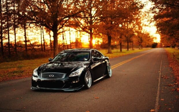 A black Infiniti G37 drives down an autumn road surrounded by fall foliage, 2K Desktop Wallpaper