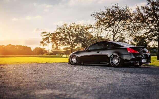 A black Infiniti G37 is parked on a gravel road near trees under a warm sunset sky, HD Desktop Wallpaper