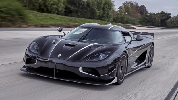 A black Koenigsegg is driving fast on a paved road surrounded by trees, 4K Desktop Wallpaper