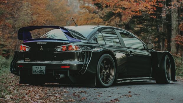 A sleek black Lancer Evo is parked on a leaf covered road surrounded by autumn trees, 4K Desktop Wallpaper