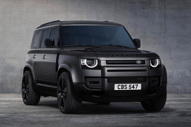 A sleek black Land Rover Defender is shown in front of a concrete wall with modern styling details, HD Desktop Wallpaper