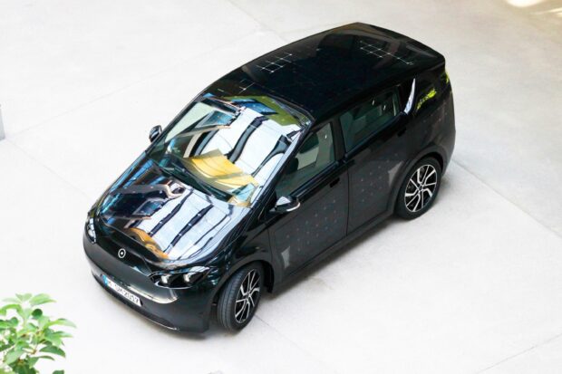 A sleek black Sono Motors car parked indoors reflecting the ceiling lights, 2K Desktop Wallpaper
