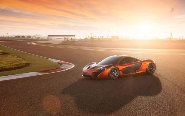 A sleek orange sports car is parked on the race track during sunset with a clear sky, 2K Desktop Wallpaper