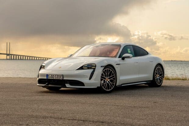 A white Porsche Taycan is parked by the water with a bridge in the background at sunset, HD Desktop Wallpaper