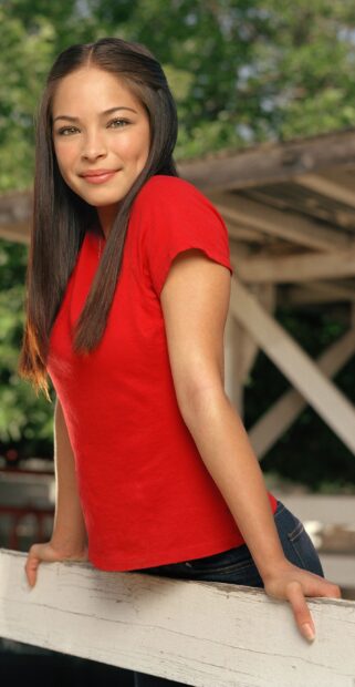 A woman in a red shirt leans on a white fence in a scene from Smallville Tv Series, 2K Phone Wallpaper