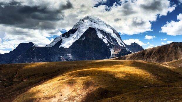 A snow covered mountain rises above golden hills in the Tibetan highlands, HD Desktop Wallpaper