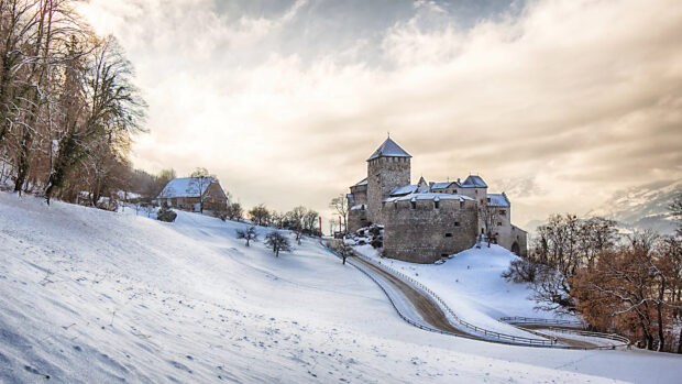 A snowy castle stands on a hill with a winding road in the Liechtenstein winter landscape, HD Desktop Wallpaper