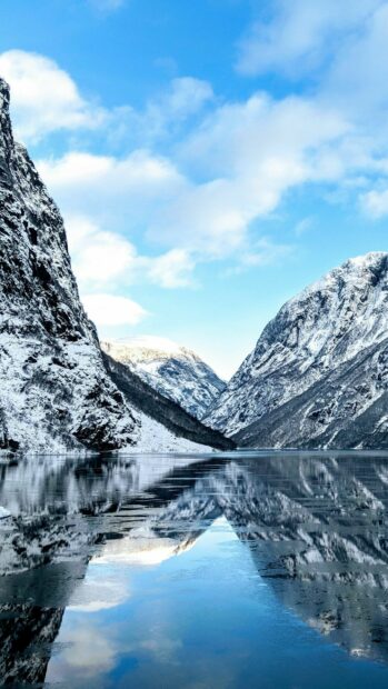 A calm lake reflects snowy mountains under a clear blue sky in Norway, 2K Mobile Wallpaper