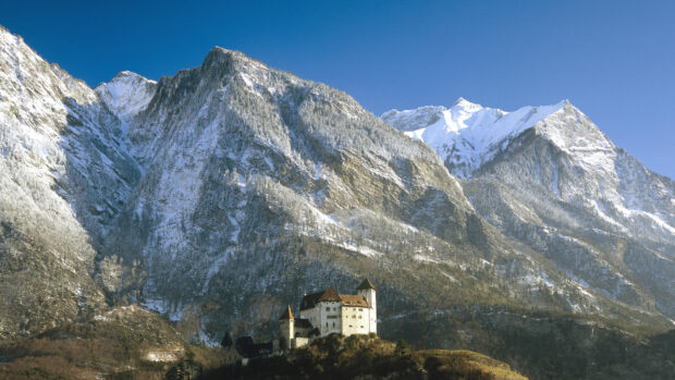 A castle rests beneath snowy mountains in Liechtenstein surrounded by clear skies, HD Desktop Wallpaper