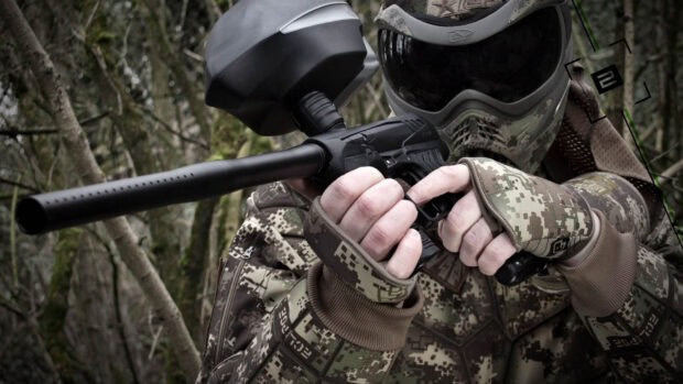 A soldier dressed in camouflage gear is aiming a paintball gun during a match, HD Desktop Wallpaper