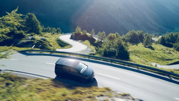 A Sono Motors vehicle drives along a winding mountain road surrounded by trees and hills, HD Desktop Wallpaper