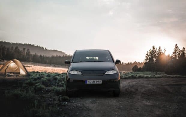 A Sono Motors vehicle is parked on a rural road with a tent nearby at sunset, HD Desktop Wallpaper