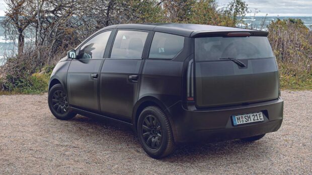 A black Sono Motors electric vehicle is parked near a coast with trees and waves in the background, HD Desktop Wallpaper