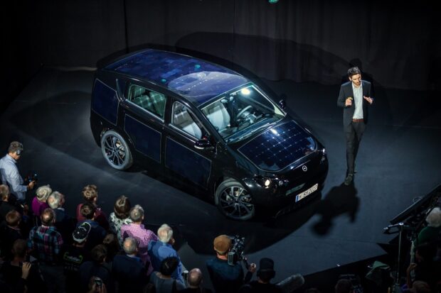A crowd watches a presenter beside a Sono Motors car with solar panels, HD Desktop Wallpaper