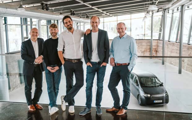 The Sono Motors team is gathered inside their facility near a small electric vehicle, 2K Desktop Wallpaper