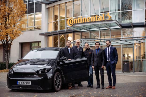 A group of men standing next to a black electric car in front of a Continental building with Sono Motors wallpapers, 2K Desktop Wallpaper