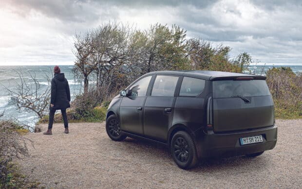 A person stands near a Sono Motors vehicle overlooking the sea on a cloudy day, HD Desktop Wallpaper