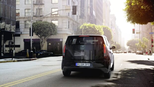 A Sono Motors vehicle is driving down an urban street with buildings and trees visible, HD Desktop Wallpaper