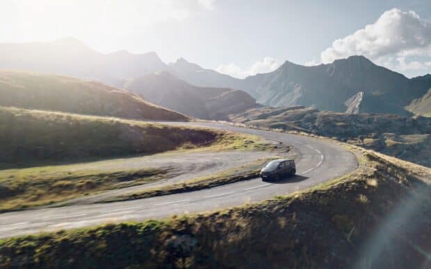 A Sono Motors vehicle is driving on a winding mountain road with clear skies, HD Desktop Wallpaper